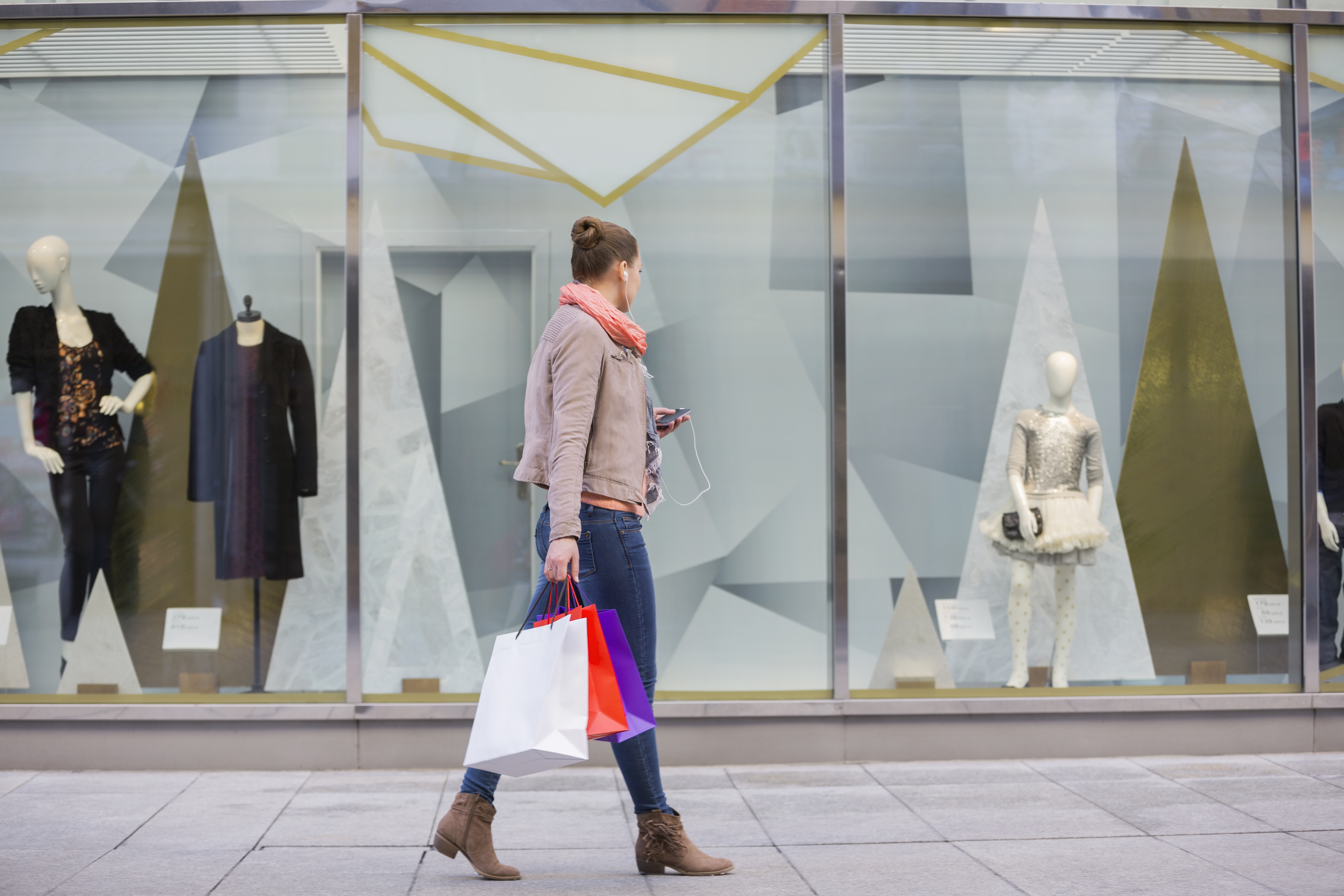Profile shot of young woman with shopping bags looking at window display